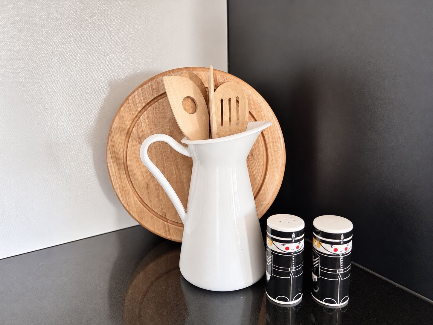 Kitchen utensils arranged in a white pitcher on a bench